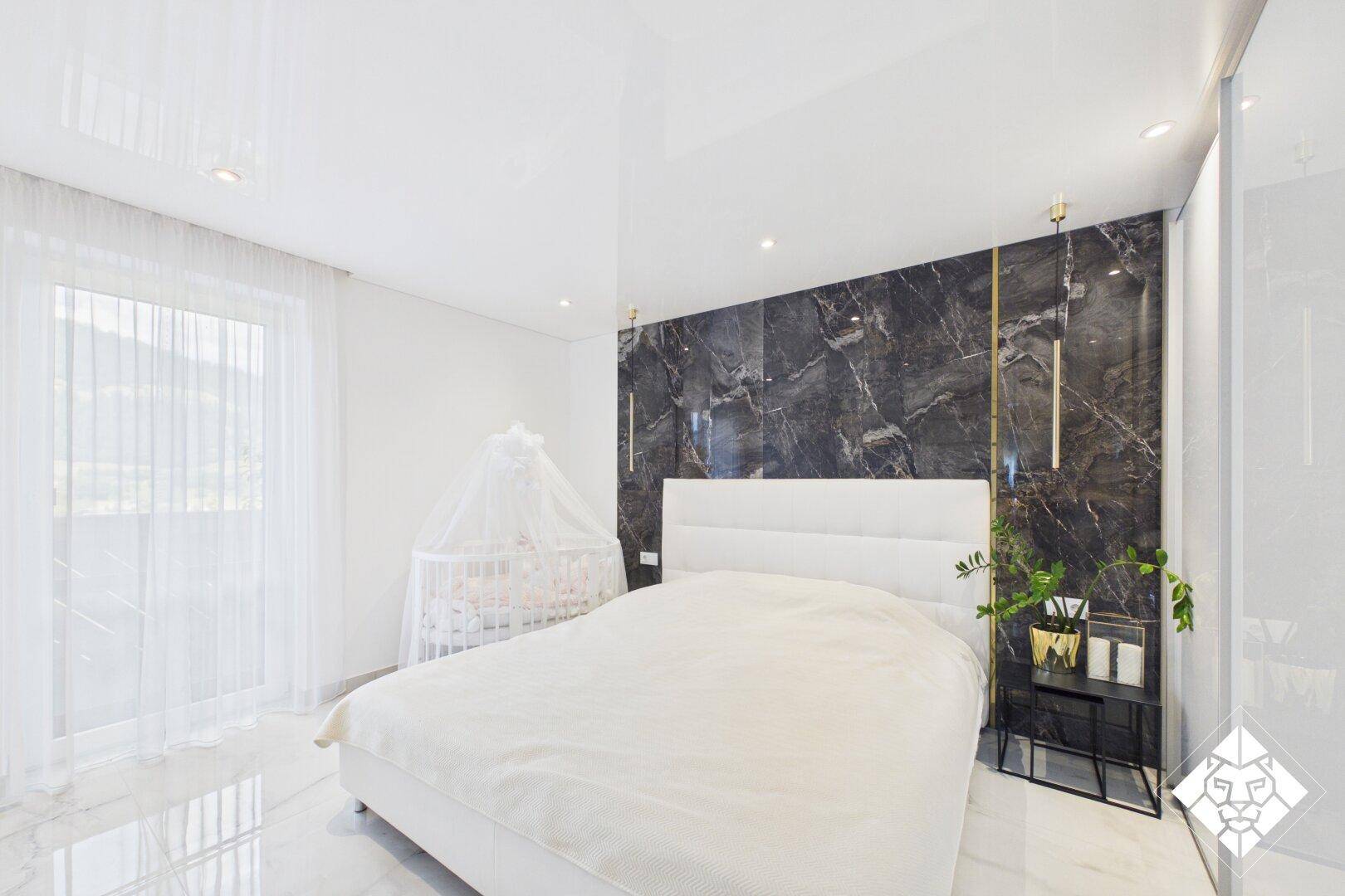 Helles Schlafzimmer mit modernem Marmor-Akzentwand, weißem Bett und Kinderbett.