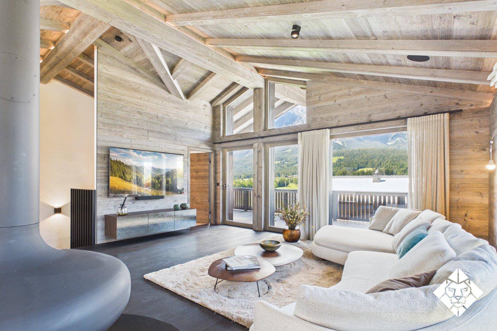 Geräumiges Wohnzimmer mit hohen Holzdecken, Kamin und Panoramablick auf die Berge.