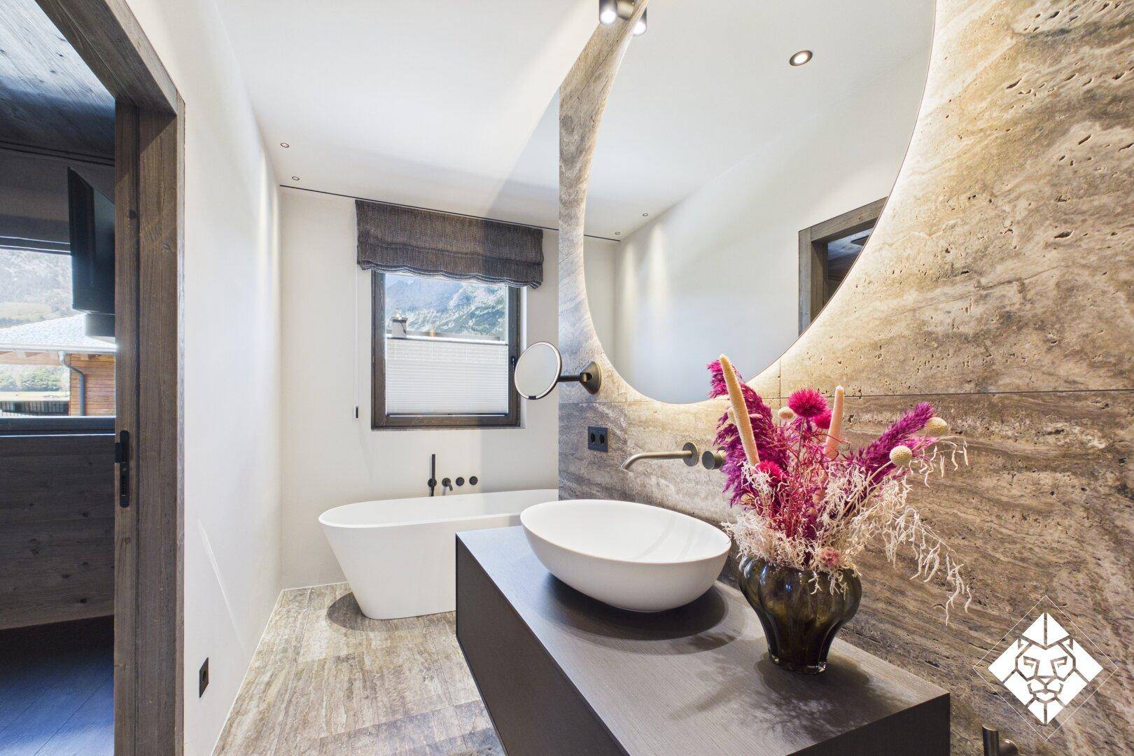 Modernes Badezimmer mit freistehender Badewanne, ovalem Waschbecken und Natursteinwand.