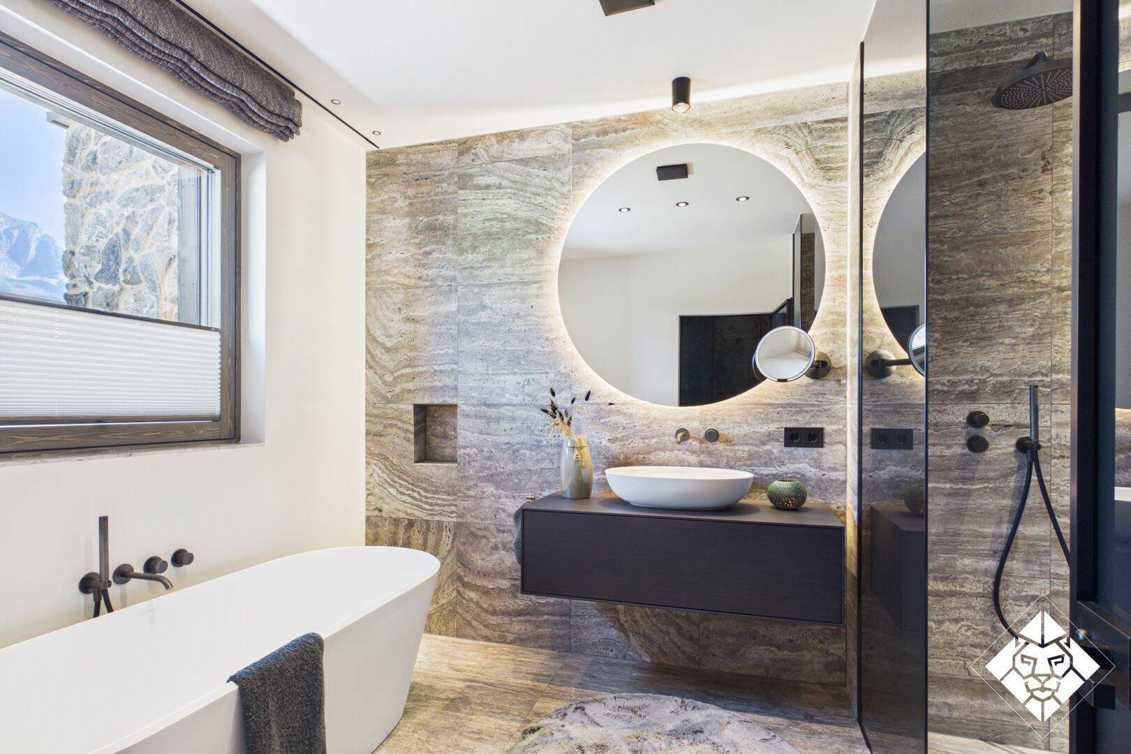 Elegantes Badezimmer mit großer Dusche, beleuchtetem Spiegel und Natursteinfliesen.