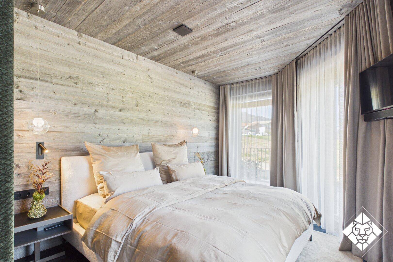 Gemütliches Schlafzimmer mit Holzwänden, Doppelbett und Zugang zum Balkon.