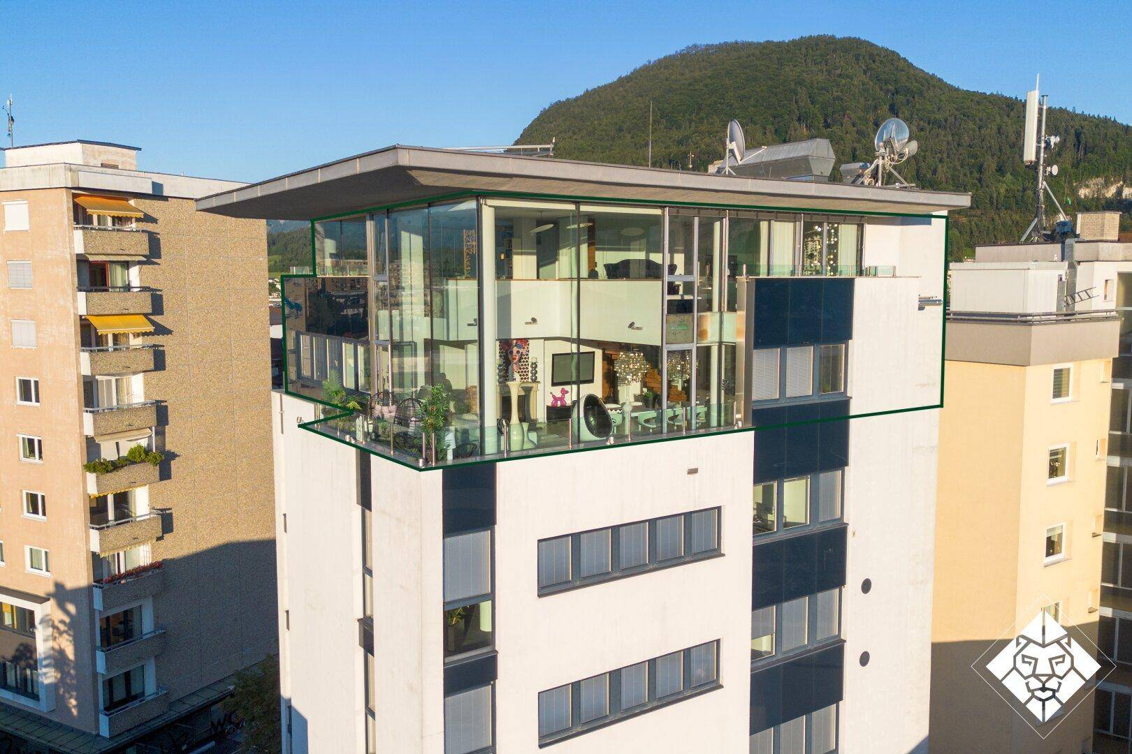 Moderne Penthouse-Wohnung mit Glasfassade und Flachdach, umgeben von Bergen in urbaner Umgebung.