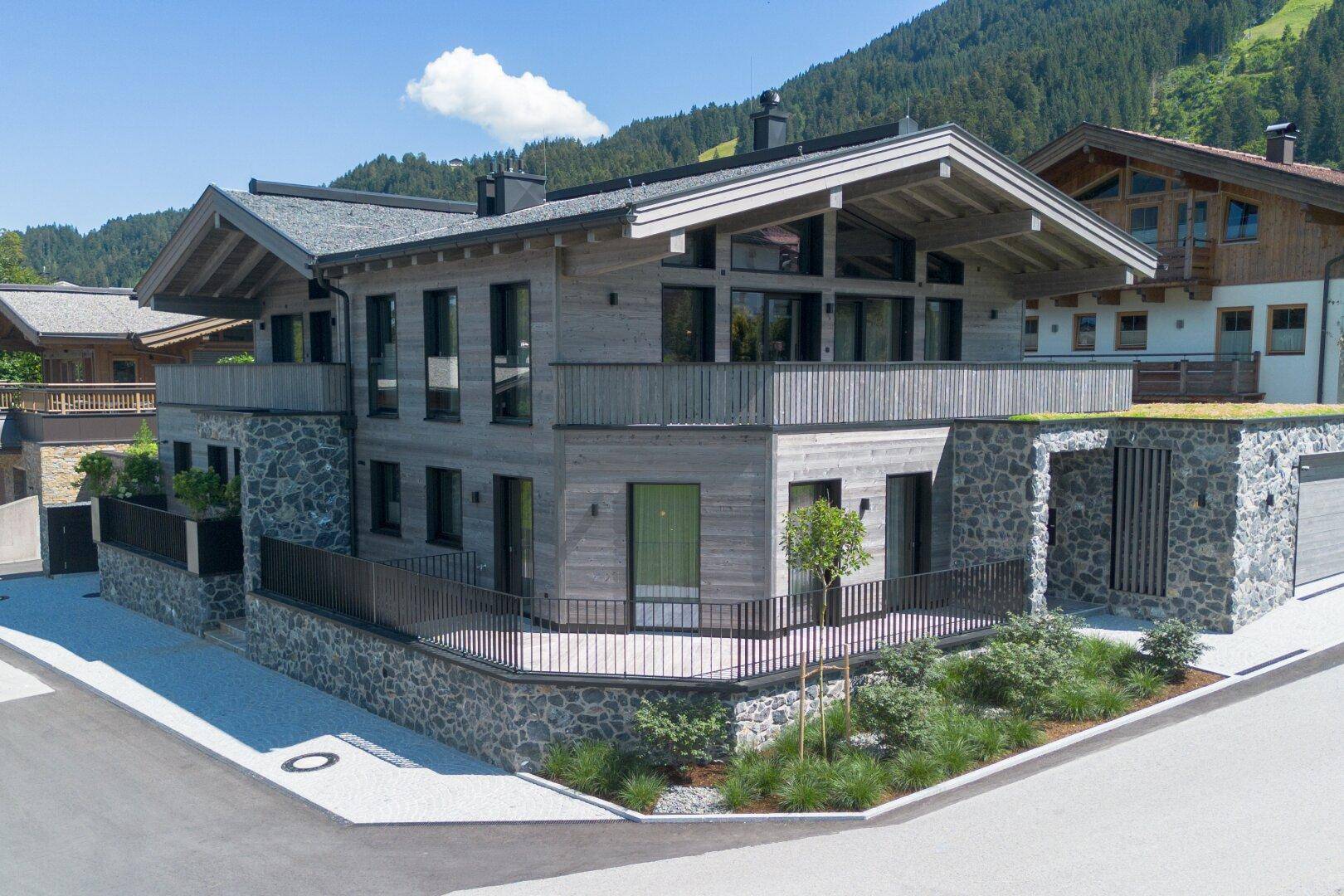 Moderne Villa im Chalet-Stil mit Holz- und Steinfassade, großen Fenstern und Bergblick.