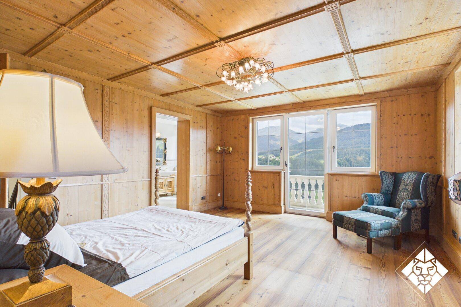 Gemütliches Schlafzimmer mit Holzvertäfelung, Holzboden und Balkonzugang mit Bergblick.