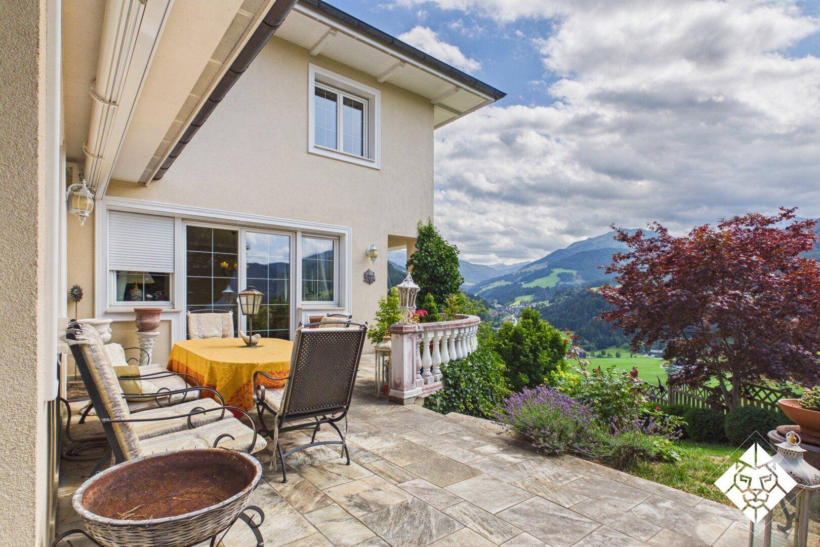 Große Steinterrasse mit Gartenmöbeln und weitem Blick über die grüne Berglandschaft.