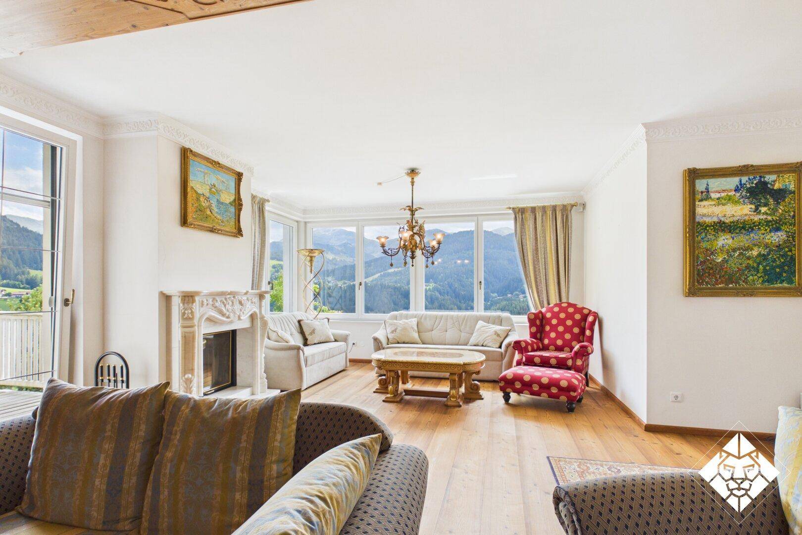 Helles Wohnzimmer mit Holzboden, Kamin und Panoramafenstern mit Bergblick.