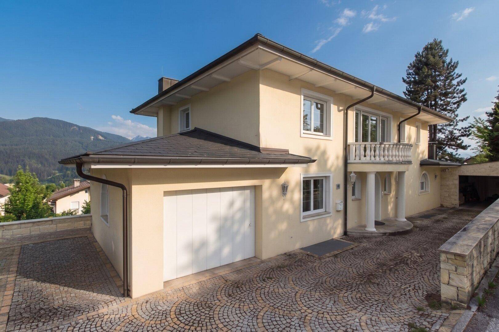Elegantes Haus mit Doppelgarage und gepflasterter Auffahrt vor bergiger Kulisse.