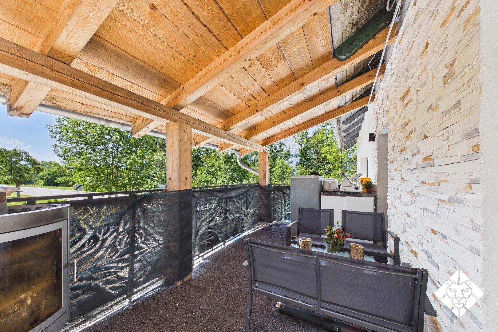 Überdachter Balkon mit Holzbalken, Sitzgelegenheiten und Blick auf die grüne Umgebung.