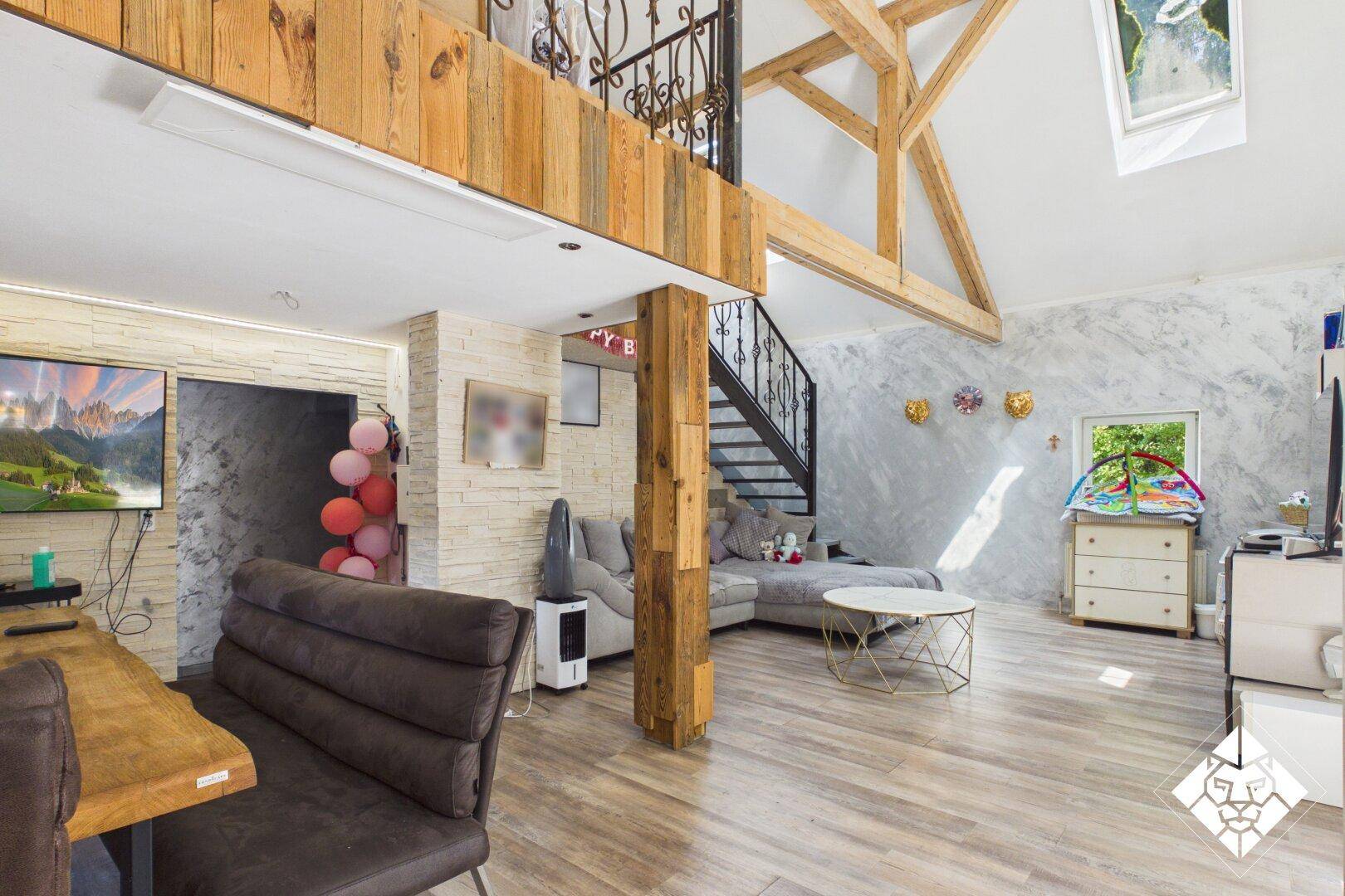 Geräumiges Wohnzimmer mit hohen Decken, sichtbaren Holzbalken und einer Treppe zum Obergeschoss.