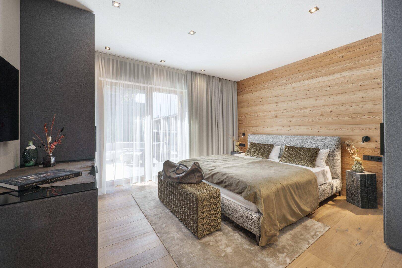 Helles Schlafzimmer mit Holzwand, Parkettboden und Zugang zu einem Außenbereich.