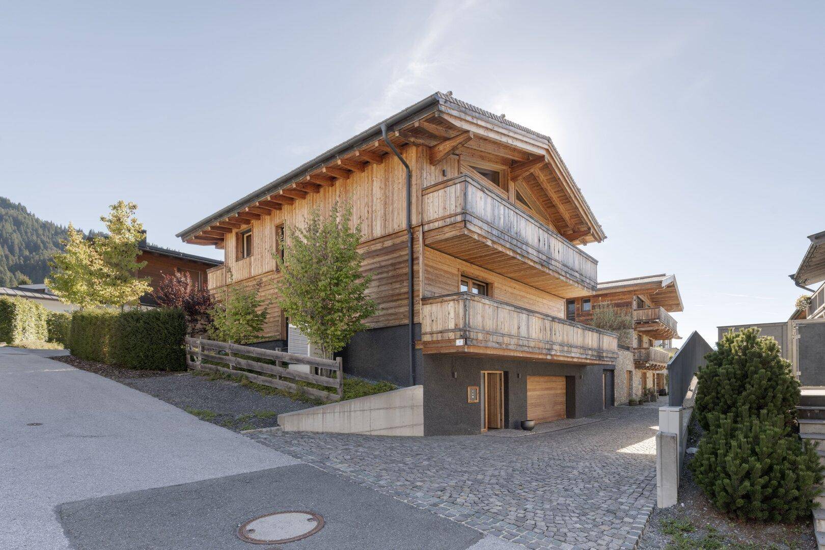 Charmantes Holzhaus mit traditioneller Architektur und gepflastertem Zugangsbereich unter blauem Himmel.