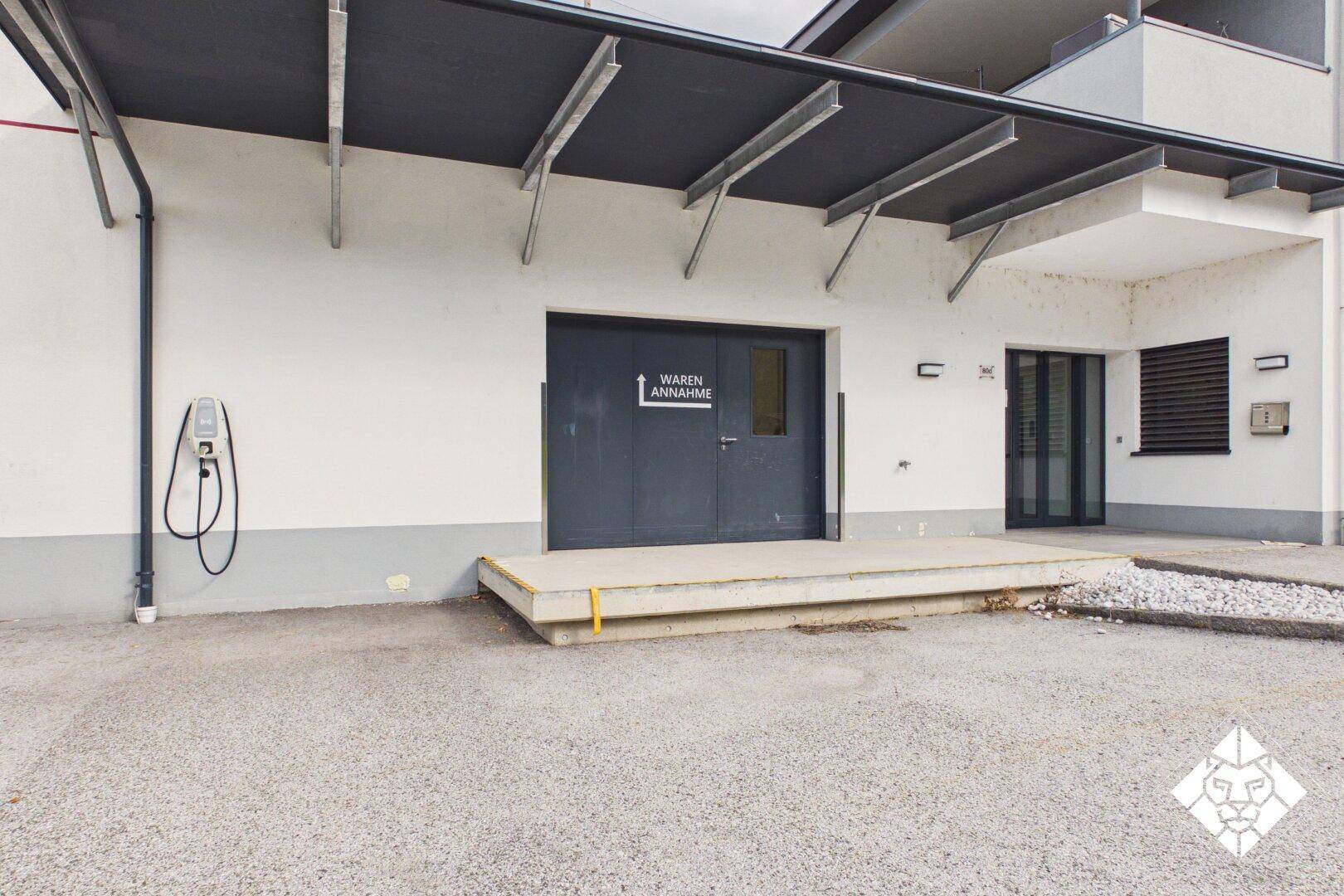Gebäudeeingang mit Laderampe, Überdachung und einer Ladestation für Elektrofahrzeuge.