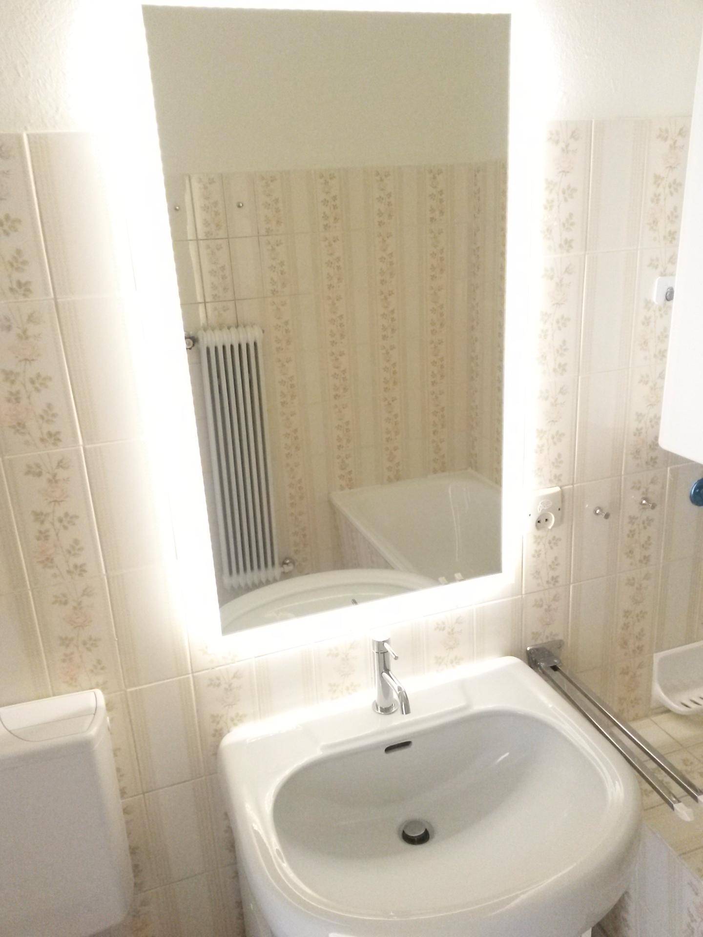 Badezimmer mit Waschbecken, beleuchtetem Spiegel und hellen Fliesen im Retro-Stil.