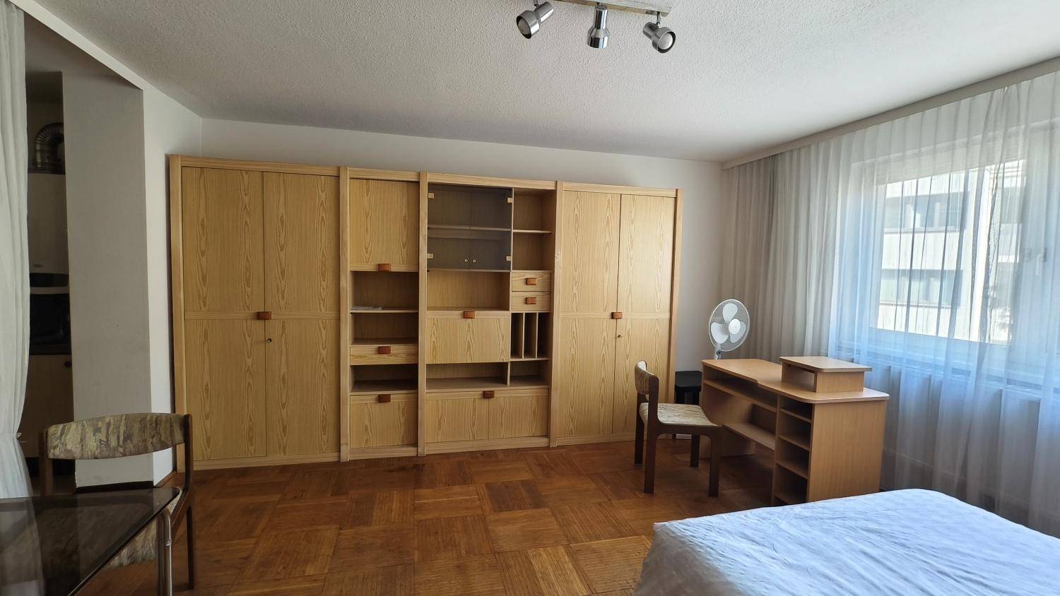 Geräumiges Schlafzimmer mit umfangreicher Holzschrankwand und viel Tageslicht durch das Fenster.
