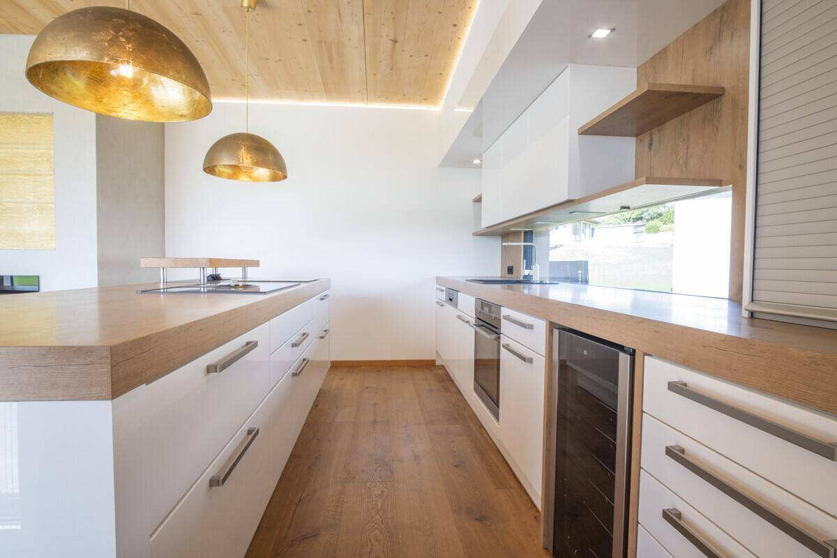 Moderne Küche mit weißen Hochglanzschränken, Holztheken und integriertem Weinkühler.