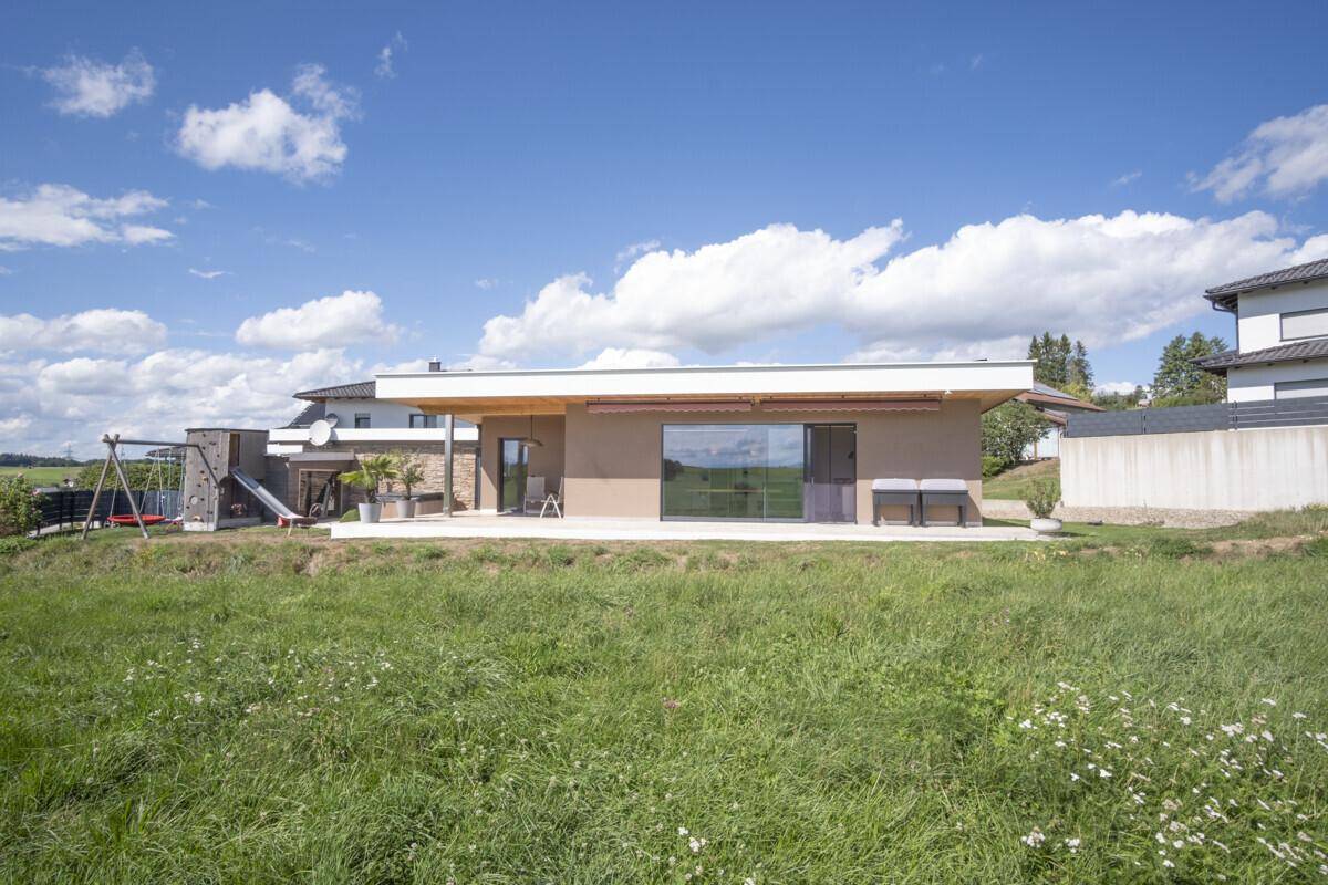 Modernes Einfamilienhaus mit Flachdach, großen Fenstern und angrenzender Terrasse mit Spielbereich.