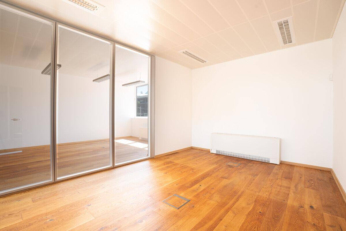Modernes Büro mit Holzboden und einer Glaswand, die den Raum optisch erweitert.