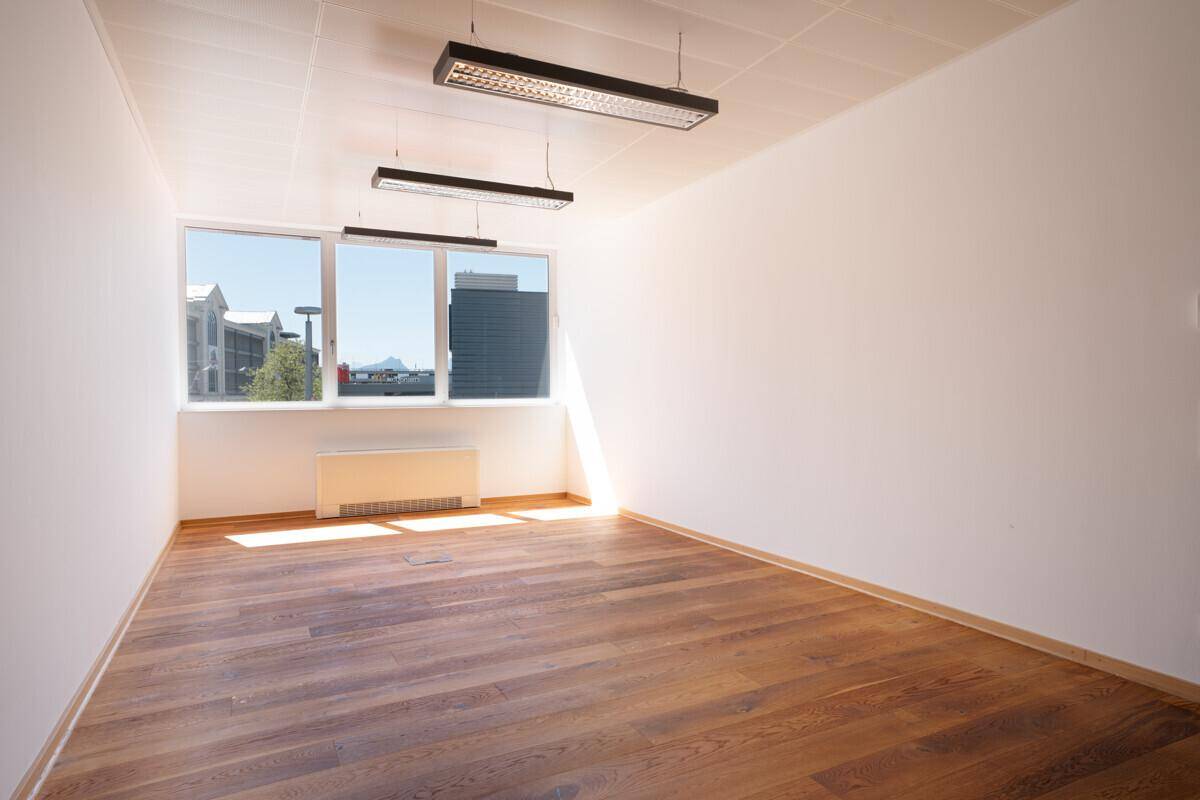 Helles Büro mit großen Fenstern, Holzboden und Blick auf die Stadt.