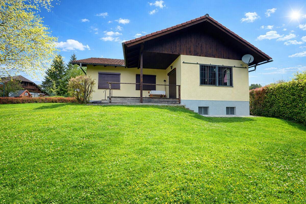 Rückansicht des Hauses mit überdachtem Eingangsbereich und großer Rasenfläche im Sonnenschein.