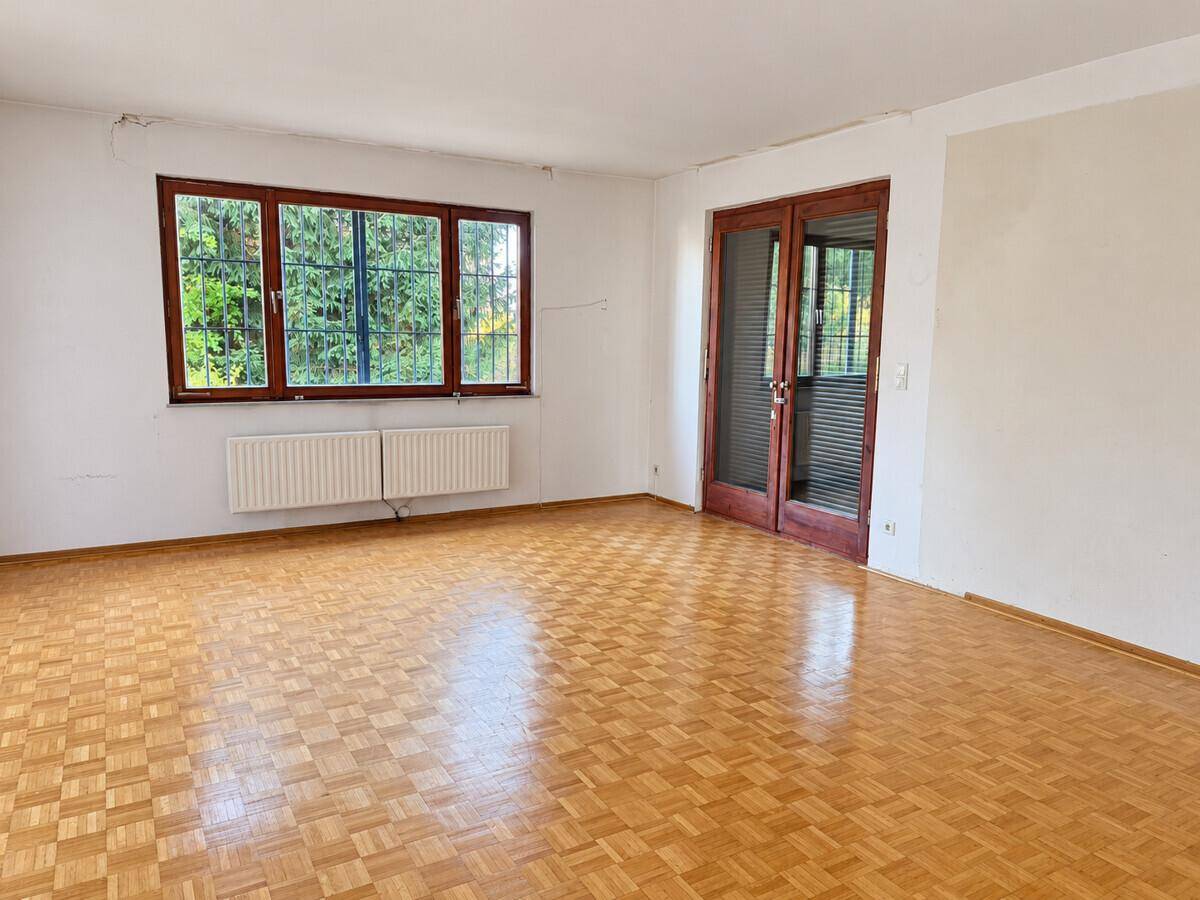 Geräumiges Wohnzimmer mit Parkettboden und Zugang zur Terrasse durch Doppeltüren.