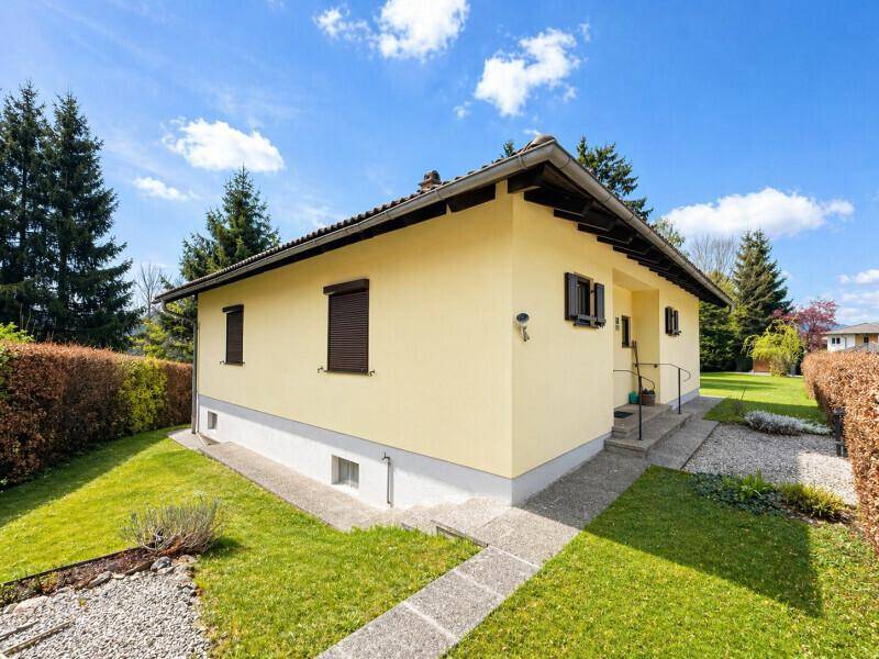 Gelbes Einfamilienhaus mit Rollläden und gepflegtem Vorgarten unter blauem Himmel.
