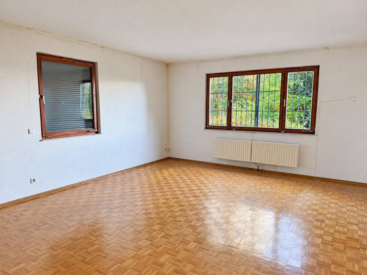 Helles Wohnzimmer mit Parkettboden und großen Fenstern mit Blick ins Grüne.
