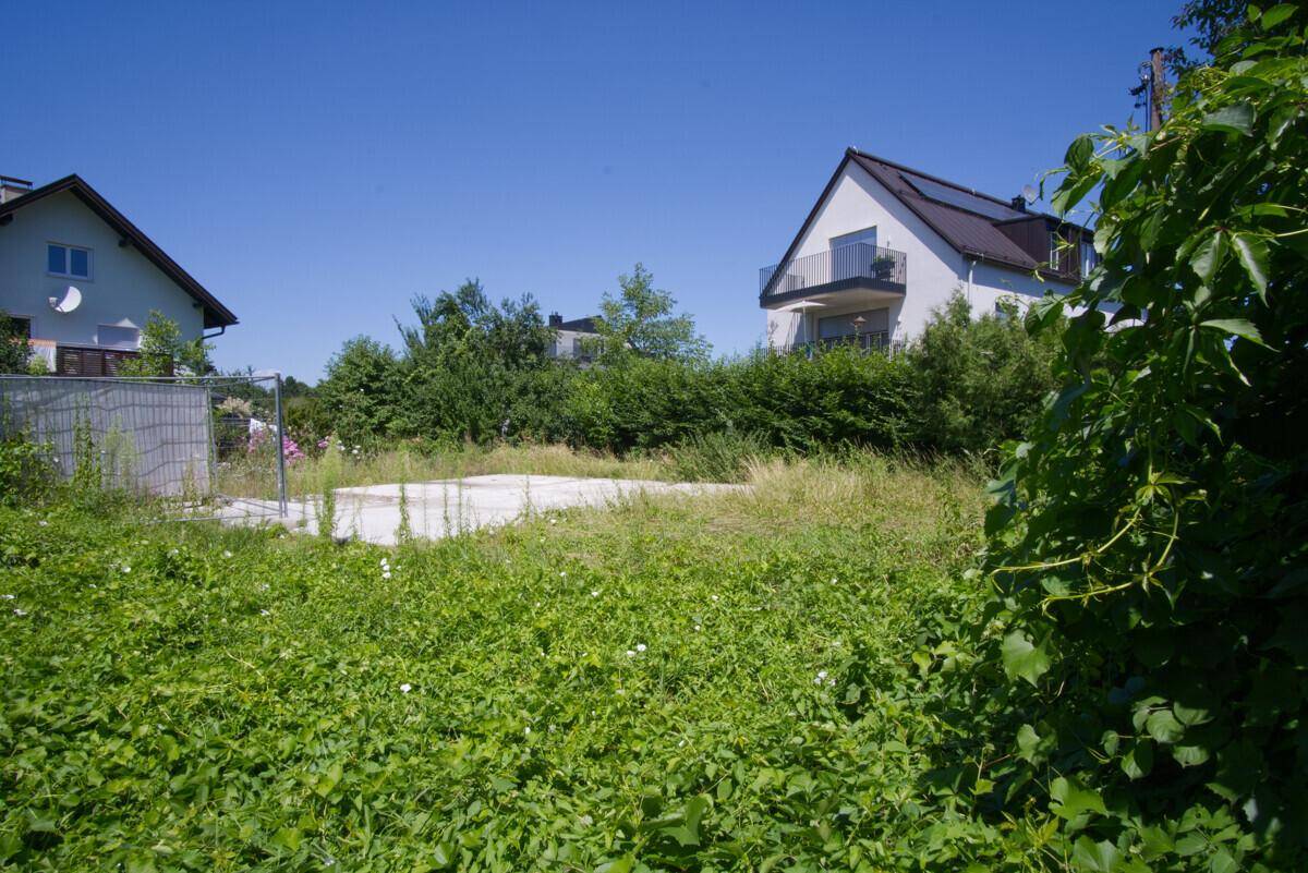 Weitläufiges, ungenutztes Grundstück mit Blick auf ein Wohnhaus mit Balkon und Solaranlage.
