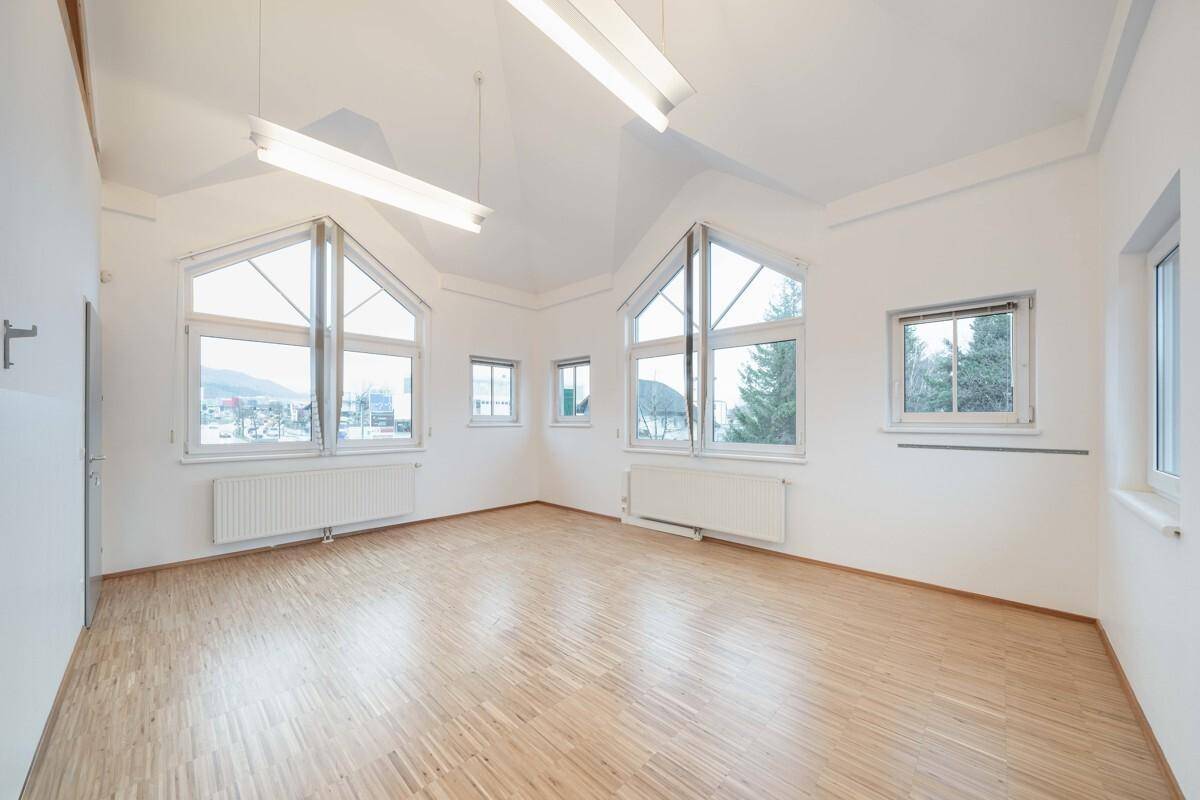 Heller Büroraum mit großen Giebelfenstern, Holzboden und hoher Decke, ideal für kreative Arbeitsbereiche.