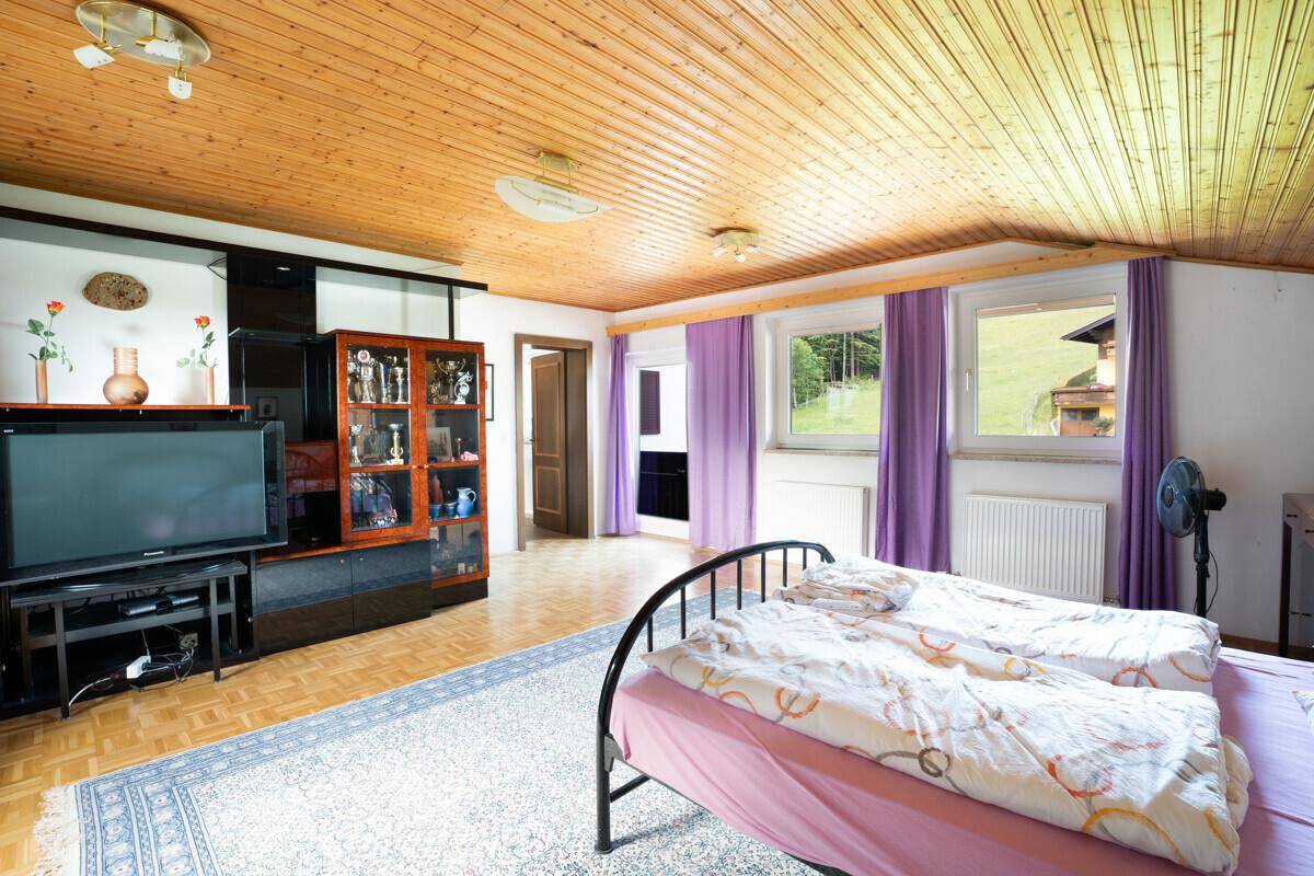Geräumiges Schlafzimmer im Dachgeschoss mit Holzdecke und Blick ins Grüne.