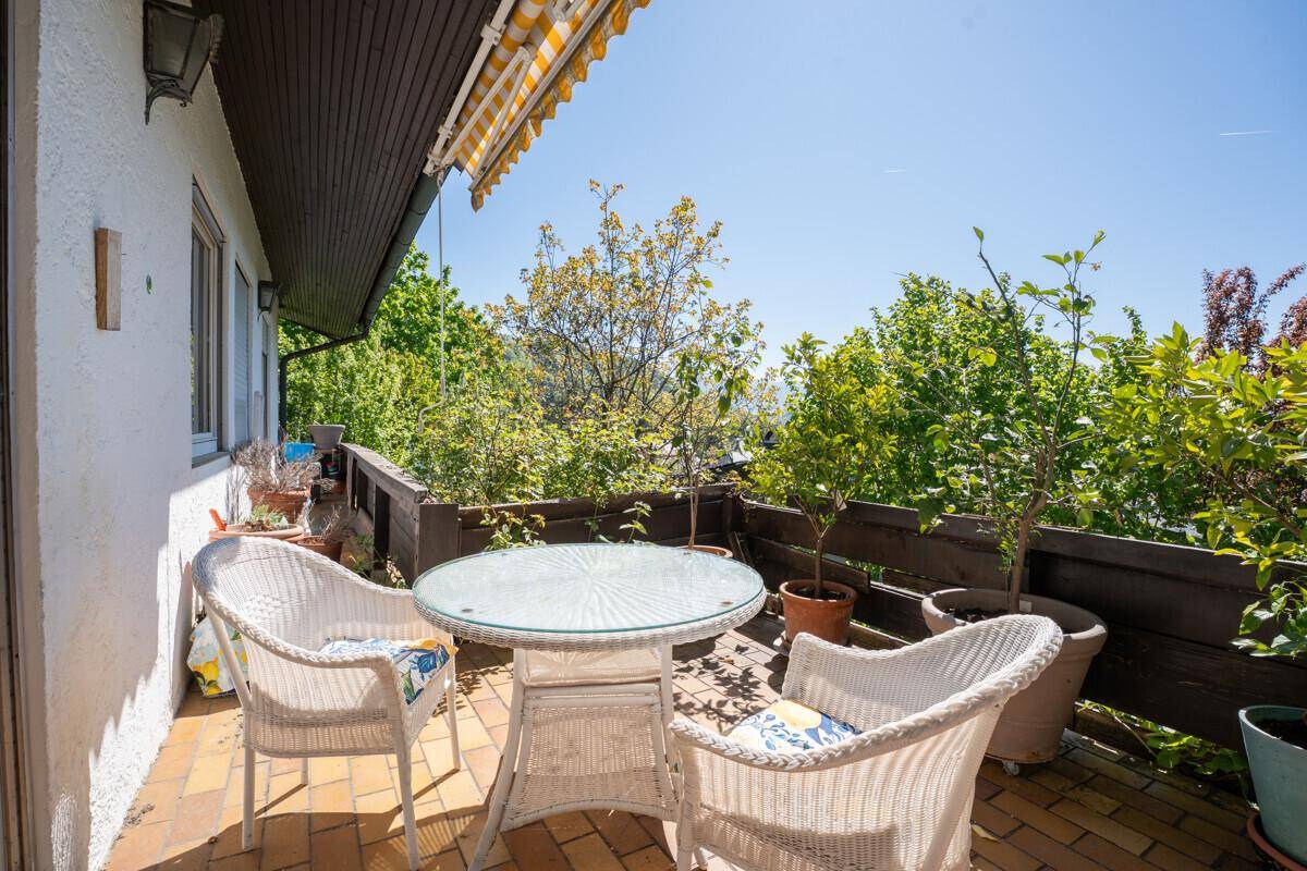 Sonniger Balkon mit Korbmöbeln und Markise, umgeben von viel Grün.