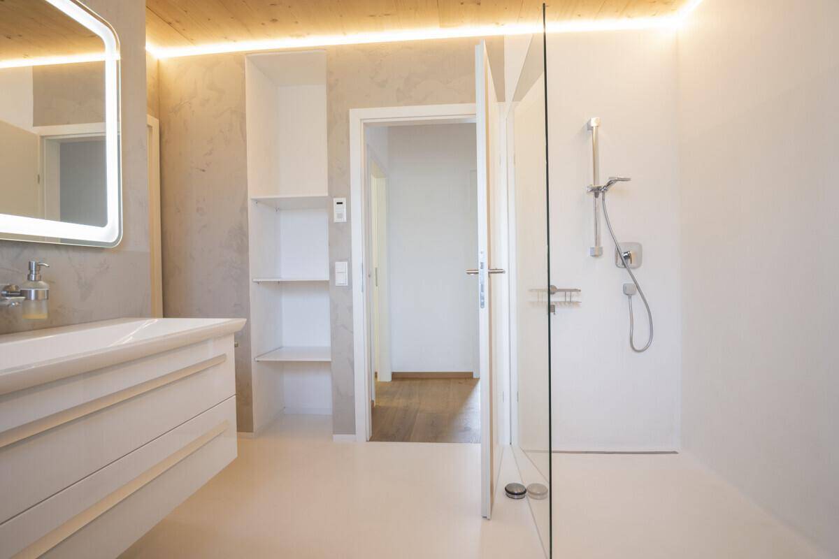 Modernes Badezimmer mit begehbarer Dusche, beleuchtetem Spiegel und praktischen Ablagen.