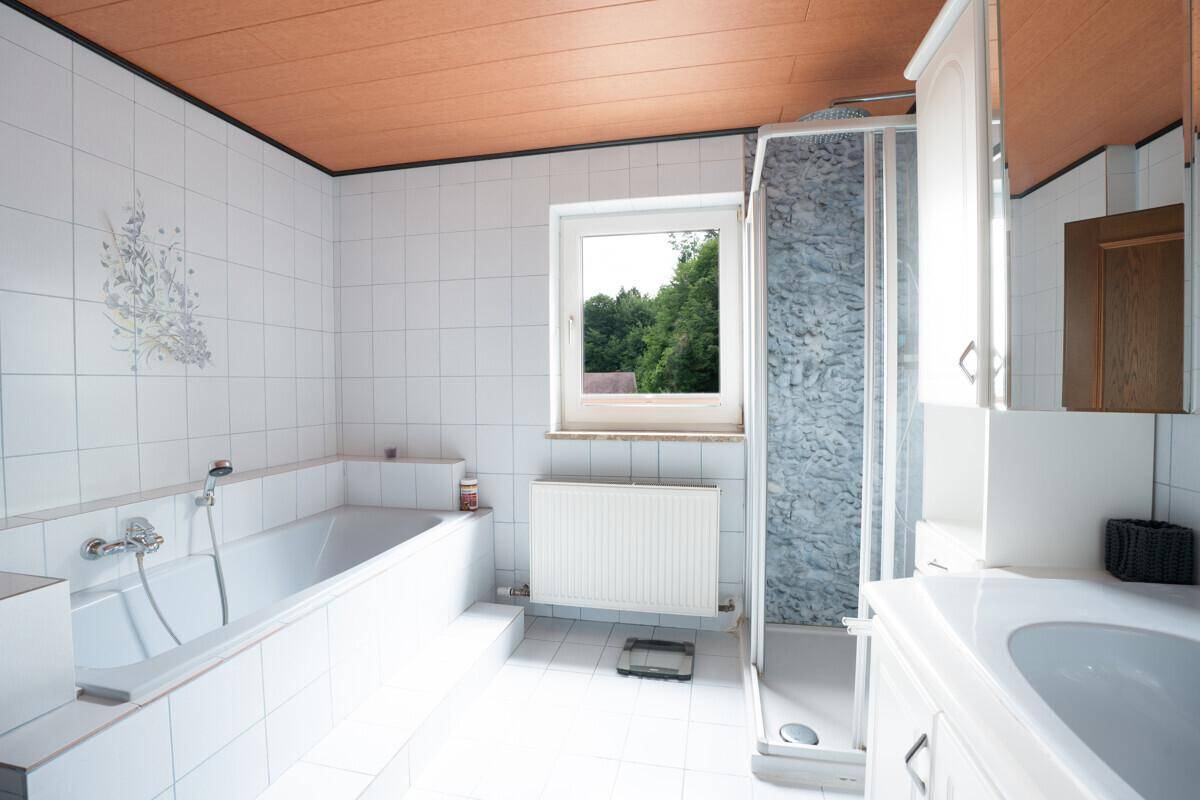 Badezimmer mit Badewanne, Duschkabine, Fenster und weißen Fliesen.