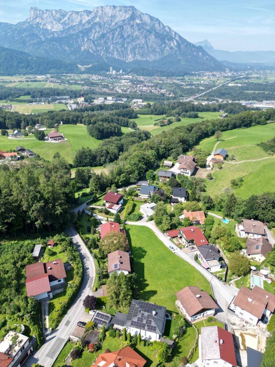 Breiter Panoramablick auf eine ländliche Siedlung mit weiten Feldern und majestätischen Bergen im Hintergrund.