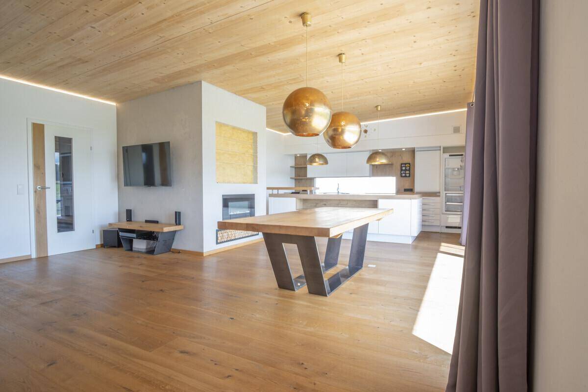 Offener Wohn-Essbereich mit Kamin, Fernseher und großen Fenstern, die viel Licht hereinlassen.
