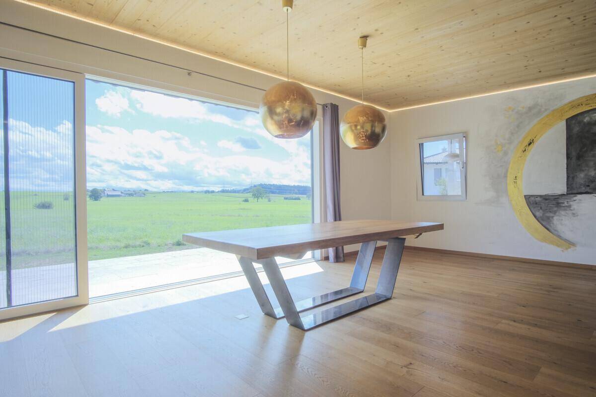 Essbereich mit modernem Holztisch, Designerleuchten und raumhohen Fenstern mit weitem Blick ins Grüne.