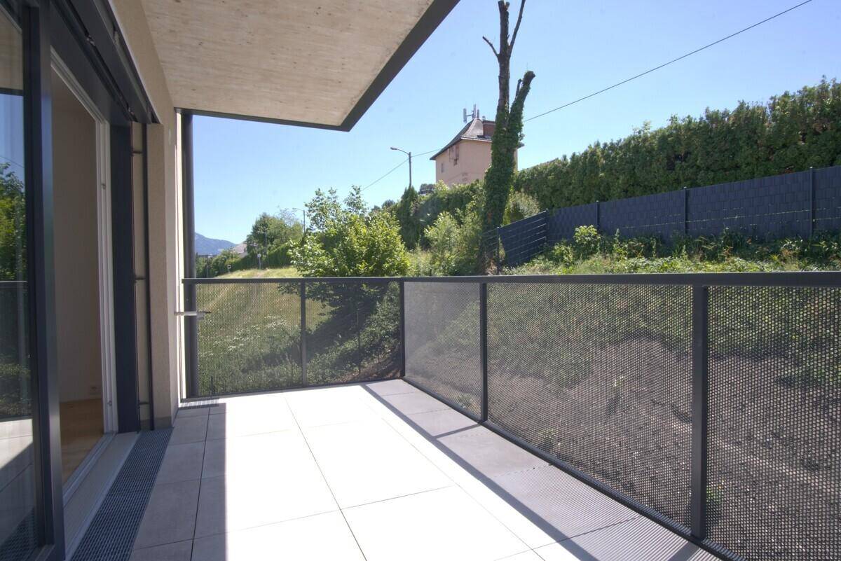 Heller Balkon mit Fliesenboden und modernem Metallgeländer, umgeben von Grün.