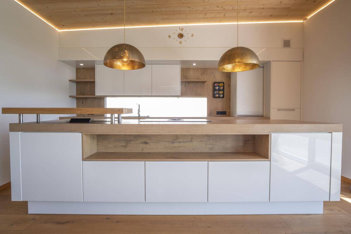 Moderne Kücheninsel mit glänzenden weißen Fronten, Holztheke und stilvollen Pendelleuchten.