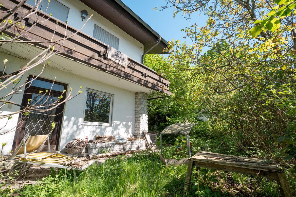 Verwilderter Gartenbereich mit viel Grün und einem Balkon im Obergeschoss.