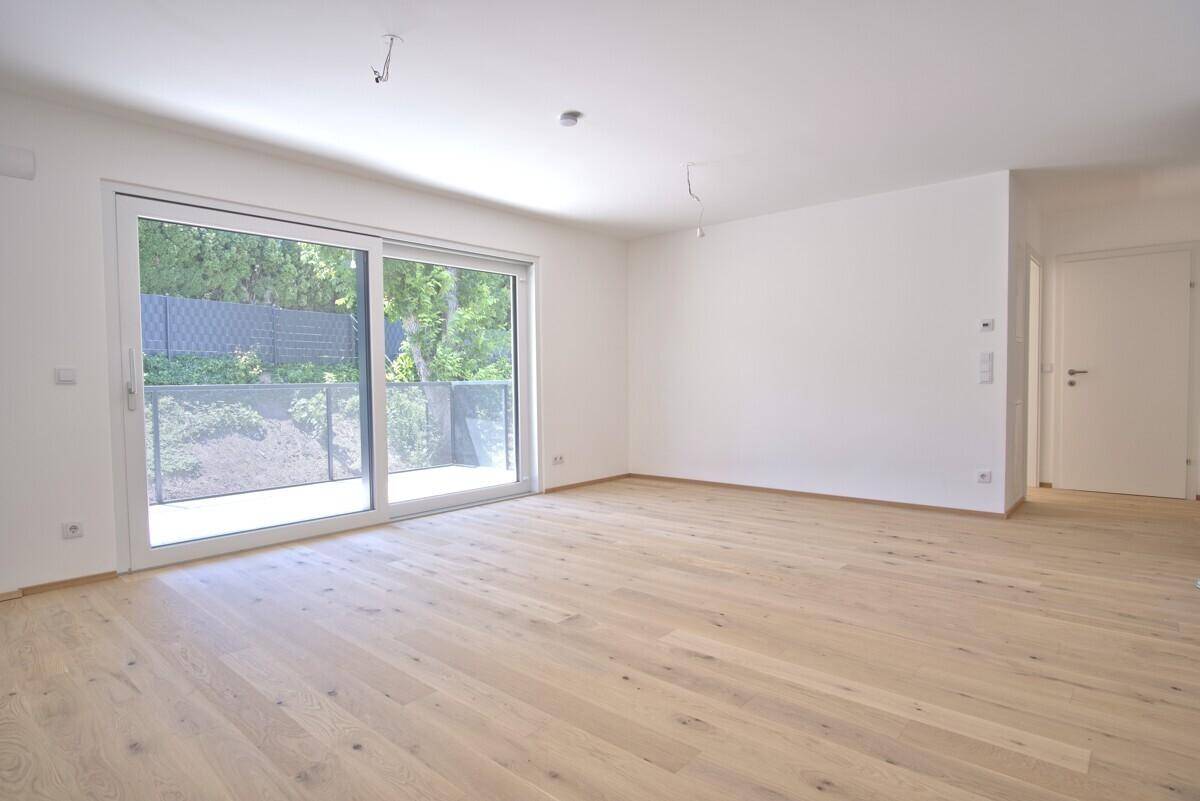 Geräumiger, heller Wohnbereich mit Parkettboden und Zugang zu einem Balkon oder Terrasse.