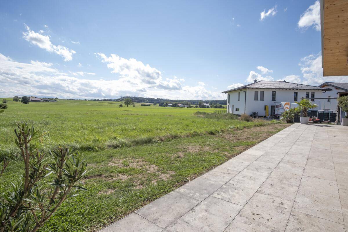 Gepflasterte Terrasse mit weitem Blick über die grüne Wiese und die umliegende Natur.