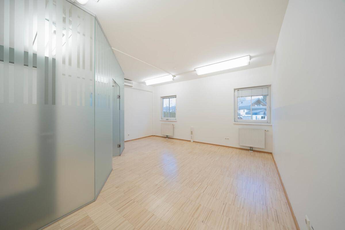 Geräumiger Büroraum mit Milchglas-Trennwänden, Holzboden und viel Tageslicht durch die Fenster.