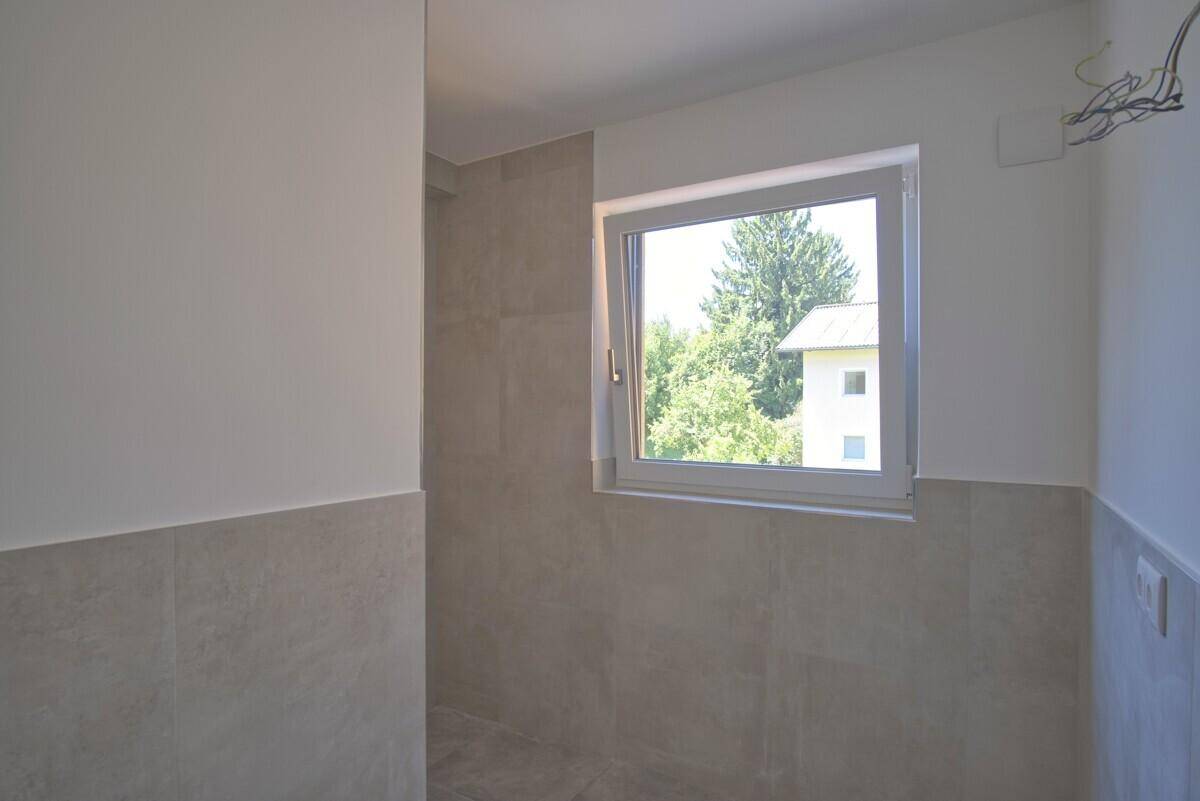 Badezimmer im Bau mit grauen Fliesen, weißen Wänden und einem Fenster für Tageslicht.