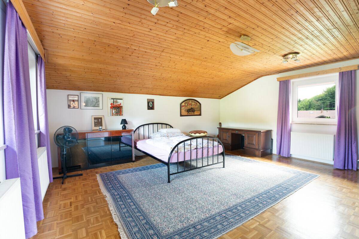 Helles Schlafzimmer im Dachgeschoss mit Holzdecke, Parkettboden und lila Vorhängen.