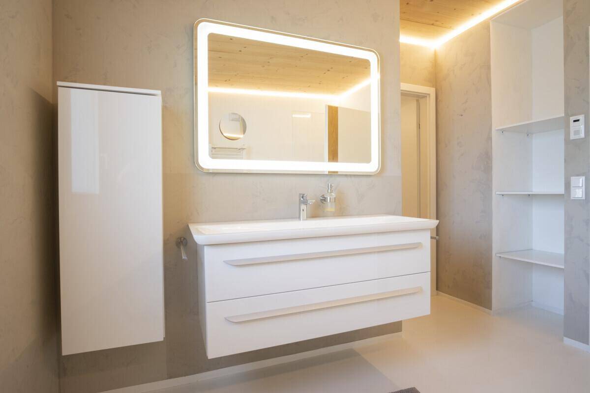 Elegantes Badezimmer mit großem beleuchtetem Spiegel, modernem Waschtisch und Holzdecke.