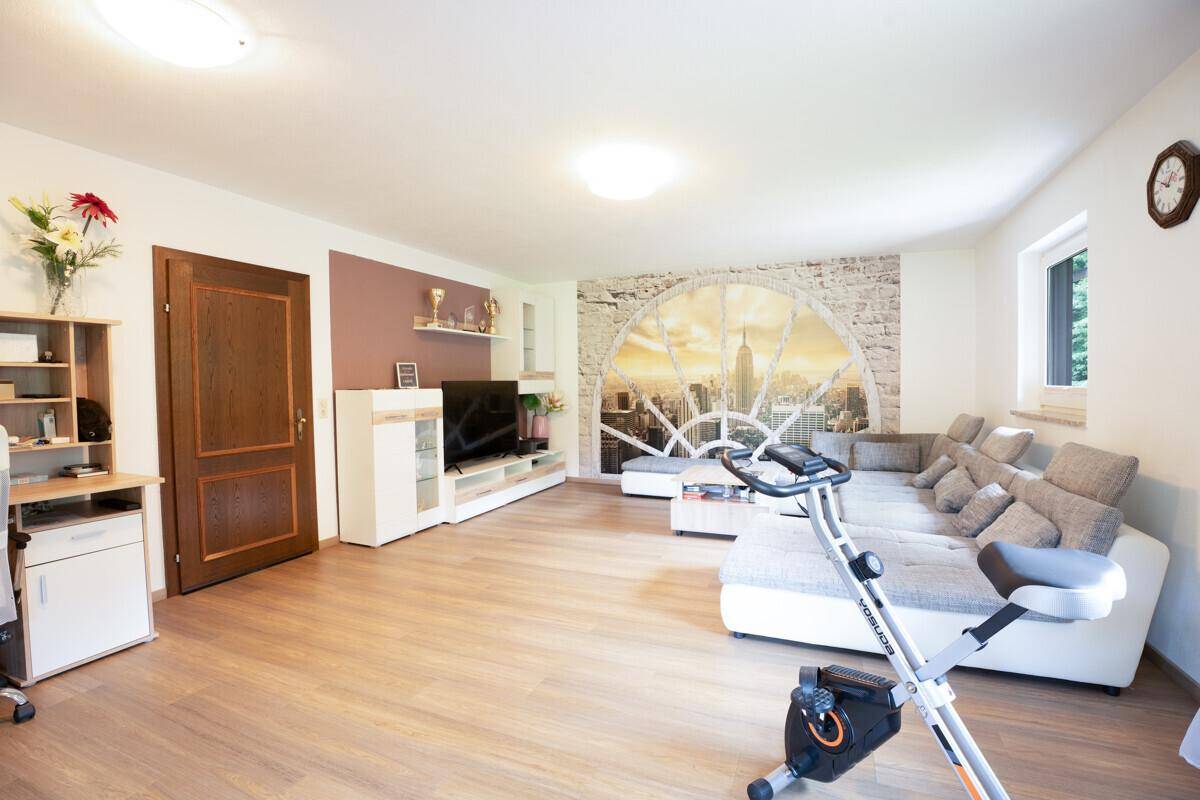 Geräumiges Wohnzimmer mit Sofa, Heimtrainer und großer Wandtapete.