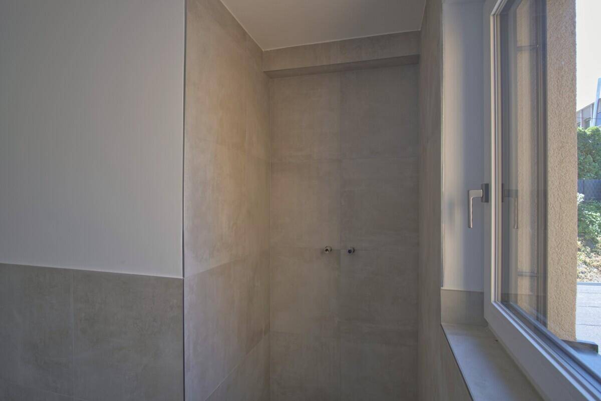 Modernes Badezimmer im Bau mit grauen Fliesen und vorbereiteten Anschlüssen für eine Dusche.
