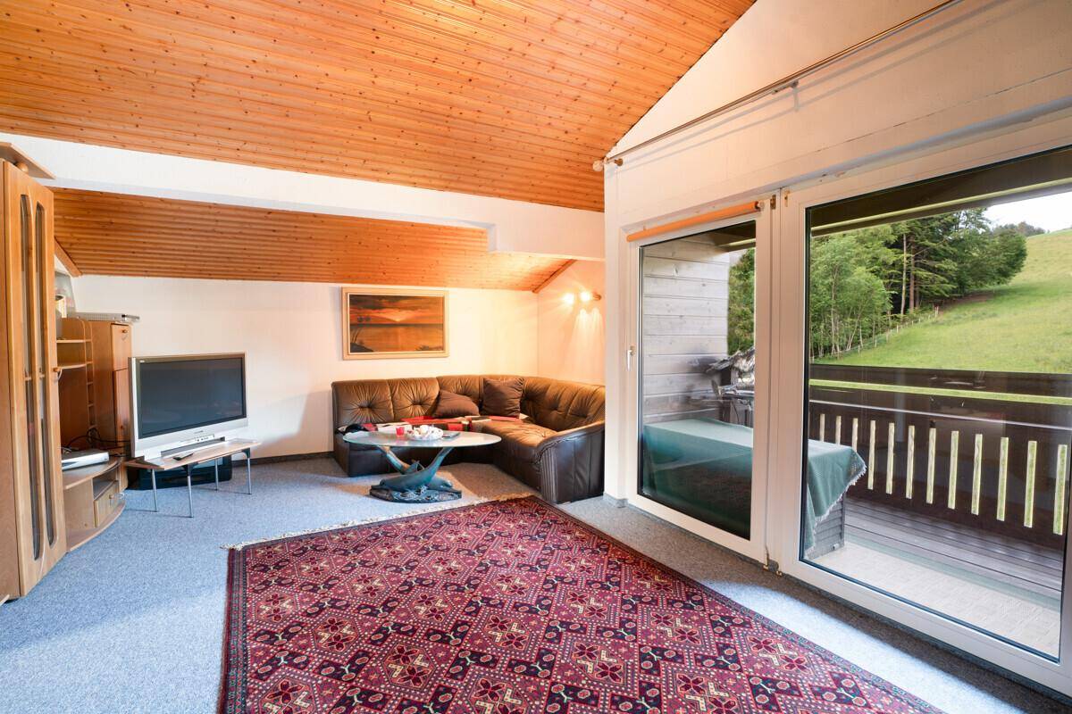 Wohnzimmer im Dachgeschoss mit Holzdecke, Sofa und Zugang zum Balkon.