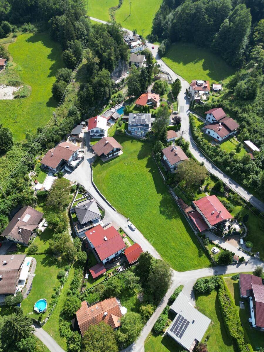 Weitläufige Luftaufnahme einer Wohnsiedlung eingebettet in grüne Hügel und Wälder.