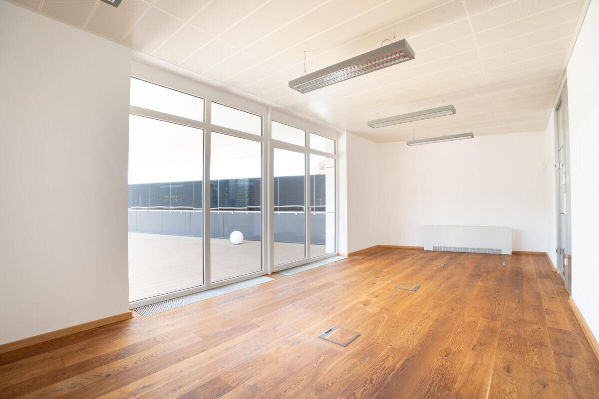 Helles Büro mit großen Fenstern, Holzboden und Zugang zu einer Außenterrasse.