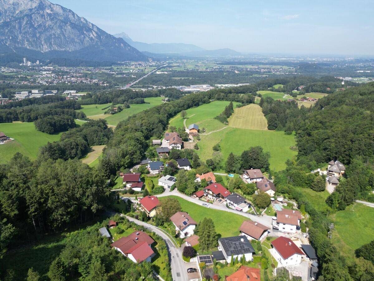 Panoramablick auf eine Wohnsiedlung mit weiten Feldern, Bergen und einer Stadt in der Ferne.